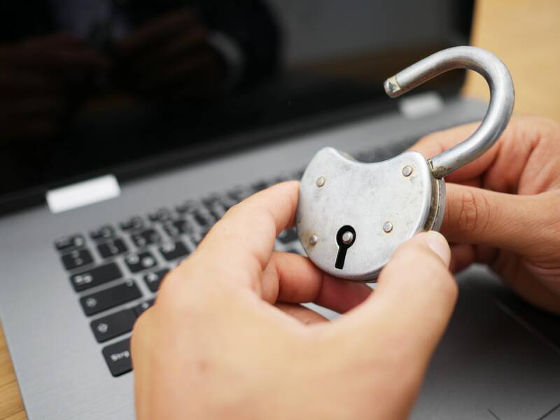 Eine Person hält ein geöffnetes Vorhängeschloss vor einem Laptop.